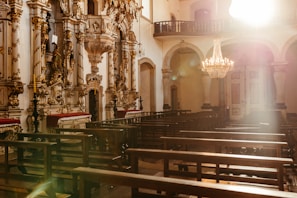 A peaceful chapel interior featuring simple, elegant decor in charcoal and soft gold, with sunlight streaming through stained glass.