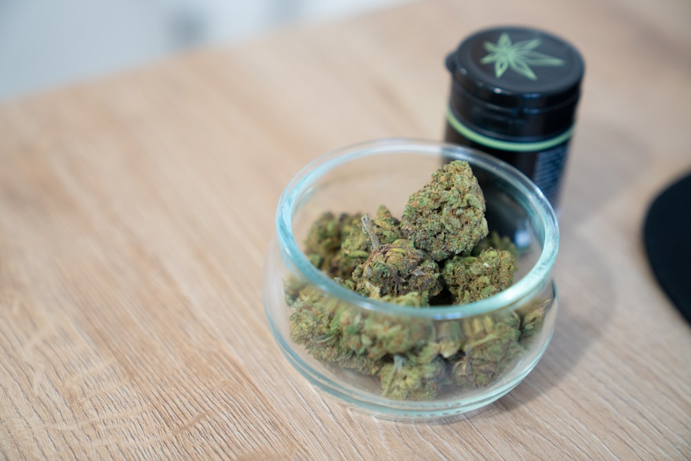 un bol en verre rempli de marijuana assis sur une table en bois