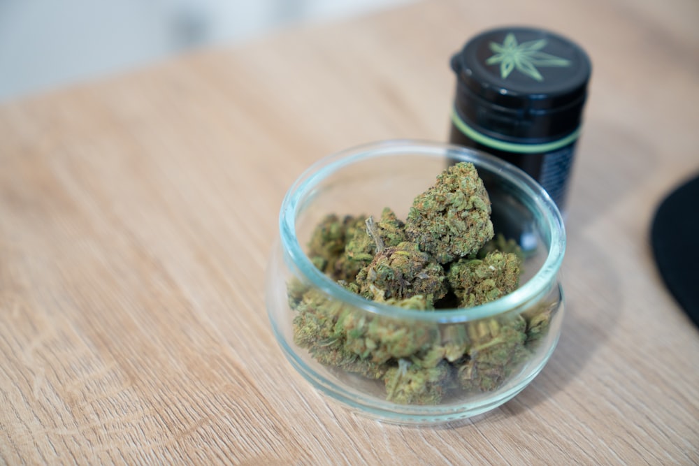 a glass bowl filled with marijuana sitting on top of a wooden table