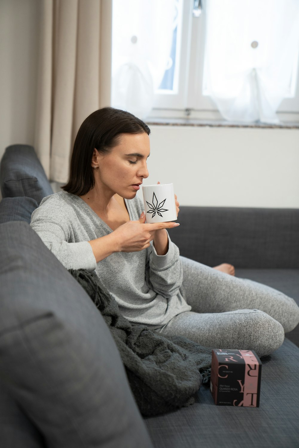 Eine Frau sitzt auf einer Couch und hält eine Kaffeetasse in der Hand