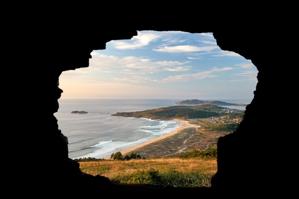 a view of a beach through a hole in a rock