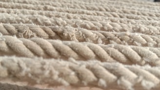 Thick, beige ropes are laid out in parallel lines, with a textured surface that appears soft yet durable. The strands of each rope are twisted tightly together, and some fibers are slightly frayed, adding to the tactile feel of the image.
