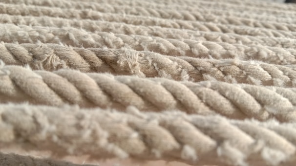 Thick, beige ropes are laid out in parallel lines, with a textured surface that appears soft yet durable. The strands of each rope are twisted tightly together, and some fibers are slightly frayed, adding to the tactile feel of the image.