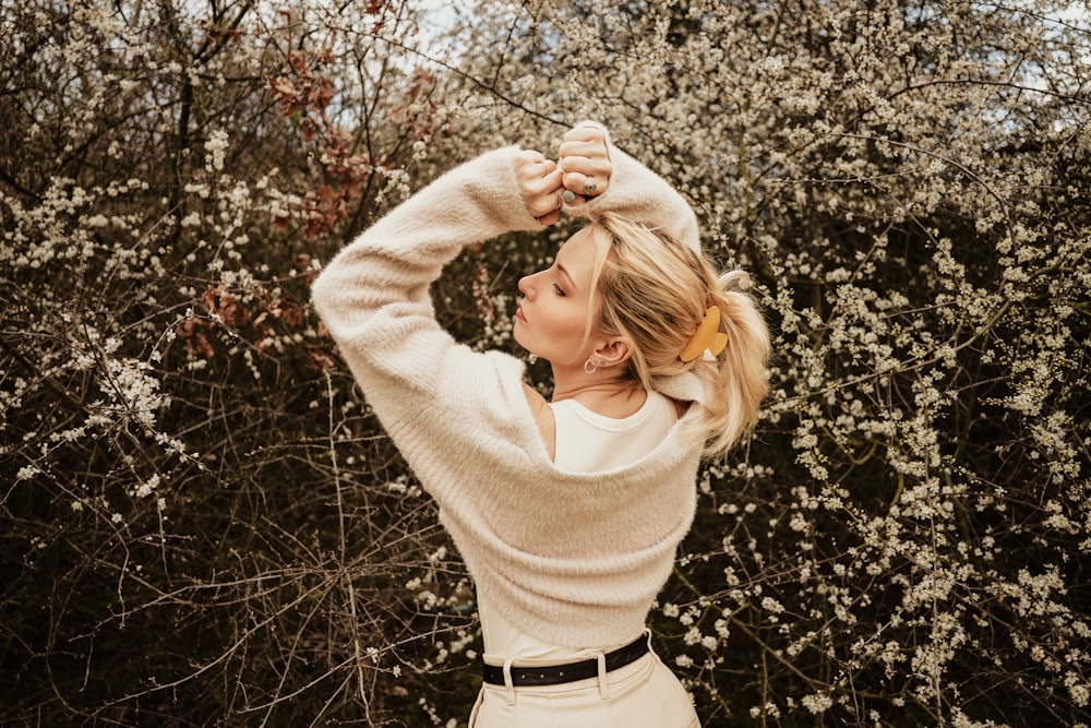 a woman standing in front of a bush with her hands on her head