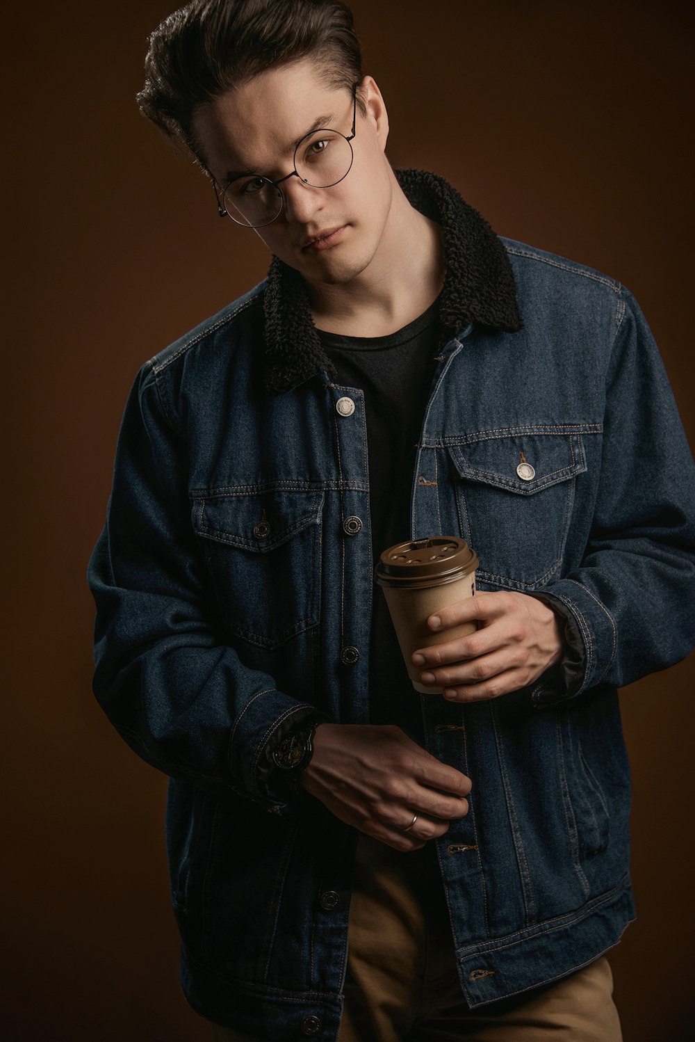 a man in a denim jacket holding a cup of coffee