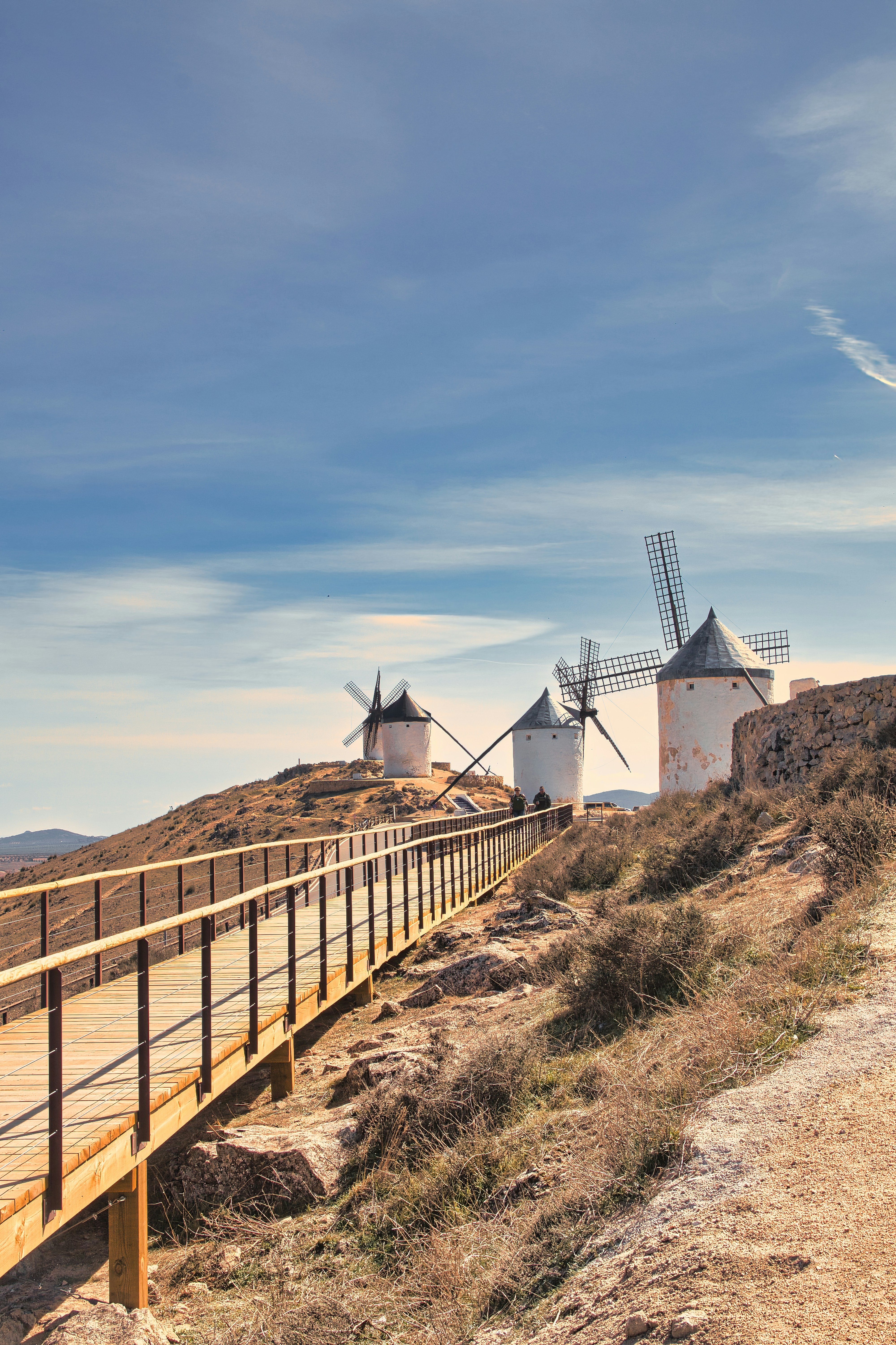 three windmills on a hill near a wooden bridge