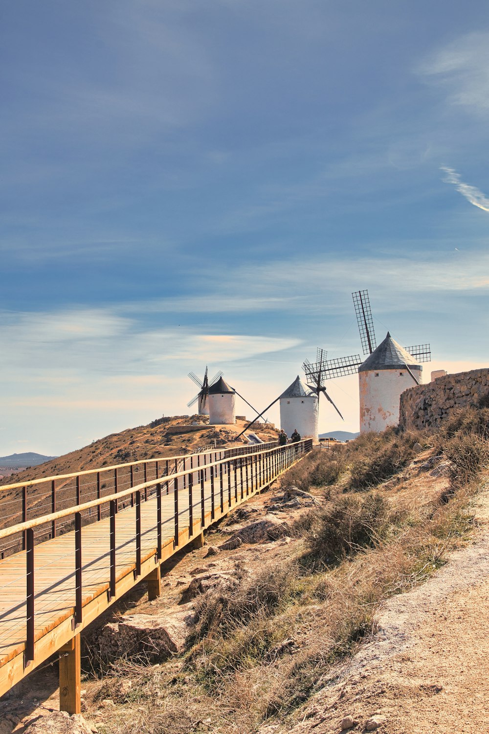 three windmills on a hill near a wooden bridge