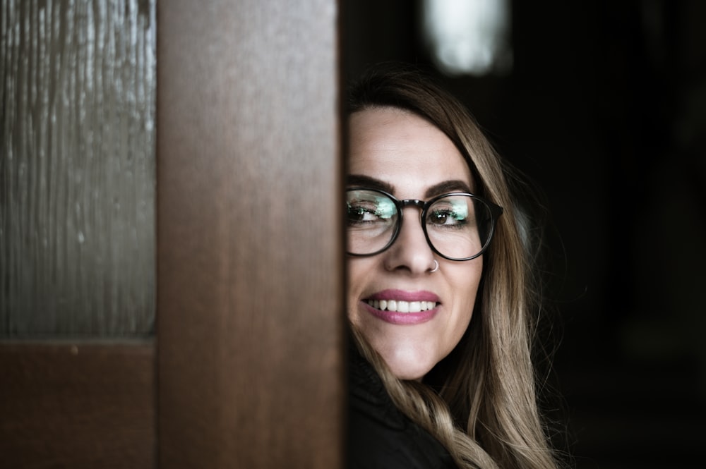 a woman wearing glasses looking out from behind a door