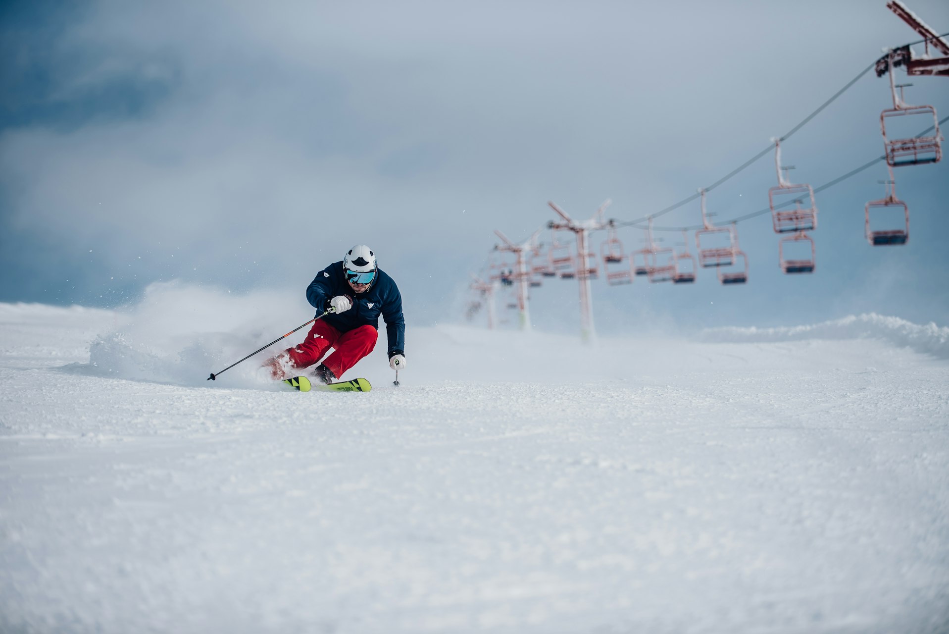 Skier carving a turn on a groomed run beneath a chairlift