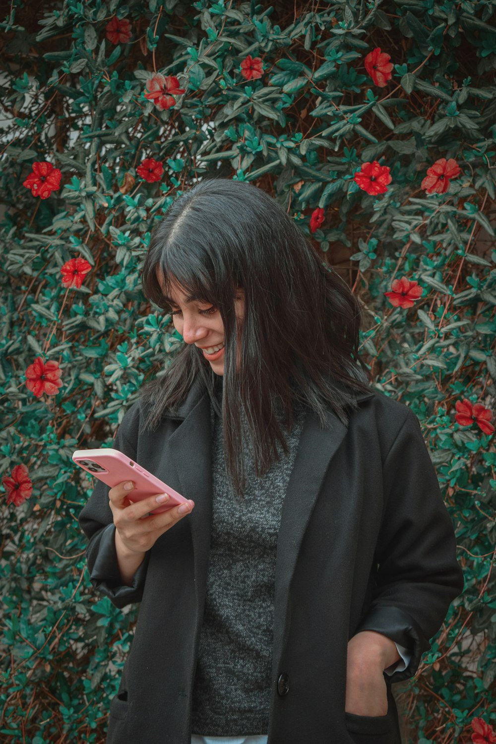 a woman standing in front of a bush looking at her cell phone