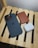 A black smartphone with a camera cluster, a brown leather wallet, and white wireless earbuds are placed on a light wooden slatted surface.