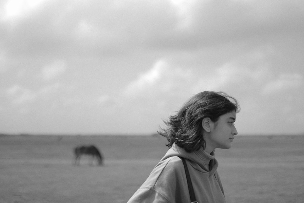 a woman standing in a field with a horse in the background