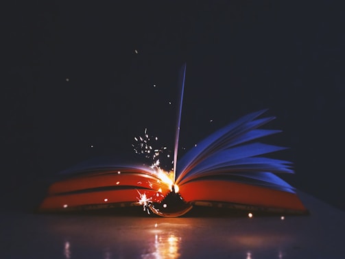 An open book with pages turning, surrounded by floating letters and symbols.