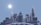 A digital cityscape with wireframe buildings in various heights and angular designs against a blue sky. The sun is positioned to the left, casting a bright glow, and the structures have a glowing outline.