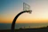A smiling basketball player holding a medal against a vibrant coastal backdrop during sunset.