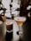 Two elegant cocktails are placed on a dark surface with a bokeh effect of warm, soft lighting in the background. The drink on the left is in a short glass with a frothy top and colorful sprinkles. The drink on the right is in a tall, stemmed glass with a smooth, creamy appearance and a decorative item resembling a star anise.