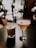 Two elegant cocktails are placed on a dark surface with a bokeh effect of warm, soft lighting in the background. The drink on the left is in a short glass with a frothy top and colorful sprinkles. The drink on the right is in a tall, stemmed glass with a smooth, creamy appearance and a decorative item resembling a star anise.