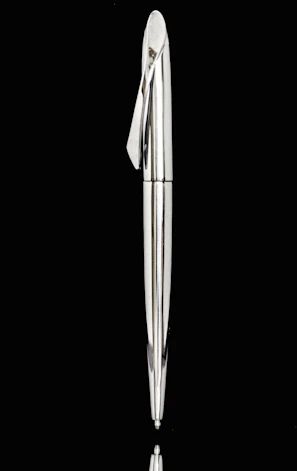 Metallic pen with a futuristic design resting on a smooth white surface, highlighted by emerald and amber reflections.