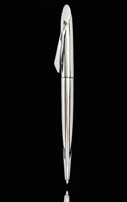 A shiny laser-engraved metal pen and badge displayed artistically on a wooden surface.