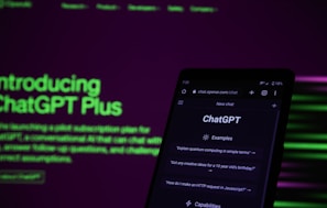 A smartphone displaying the ChatGPT web interface is positioned against a dark background with bright green and purple text promoting ChatGPT Plus. The screen of the phone shows examples of prompts such as 'Explain quantum computing in simple terms.' The lighting is dim, contrasting with the illuminated text and phone screen.