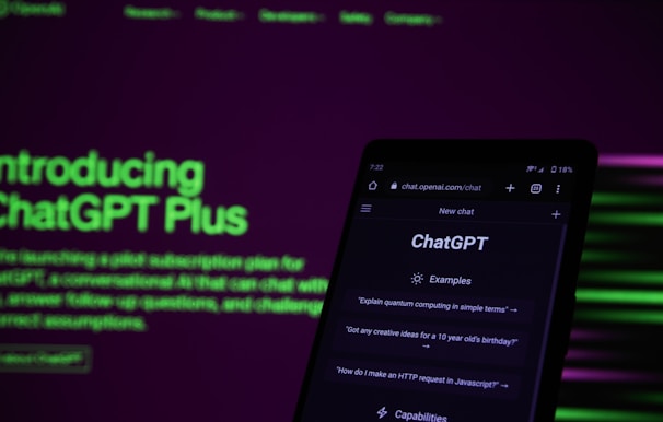 A smartphone displaying the ChatGPT web interface is positioned against a dark background with bright green and purple text promoting ChatGPT Plus. The screen of the phone shows examples of prompts such as 'Explain quantum computing in simple terms.' The lighting is dim, contrasting with the illuminated text and phone screen.