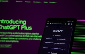 A smartphone displaying the ChatGPT web interface is positioned against a dark background with bright green and purple text promoting ChatGPT Plus. The screen of the phone shows examples of prompts such as 'Explain quantum computing in simple terms.' The lighting is dim, contrasting with the illuminated text and phone screen.