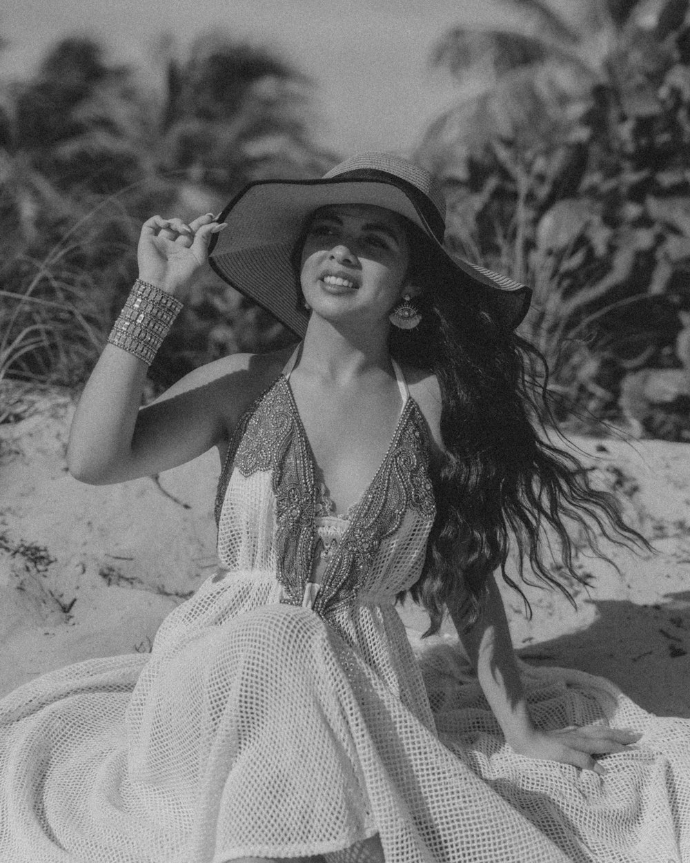 a woman in a dress and hat sitting on a beach
