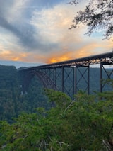 An elegant bridge arching over a river, surrounded by lush greenery and a setting sun.