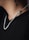 A close-up of a person's neck featuring a silver chain with a pendant shaped like a skull. The person is wearing a black shirt, and there is a black tattoo visible on the neck.