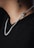 A close-up of a person's neck featuring a silver chain with a pendant shaped like a skull. The person is wearing a black shirt, and there is a black tattoo visible on the neck.