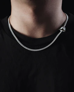 Close-up of a man wearing a sleek silver chain necklace with a minimalist pendant