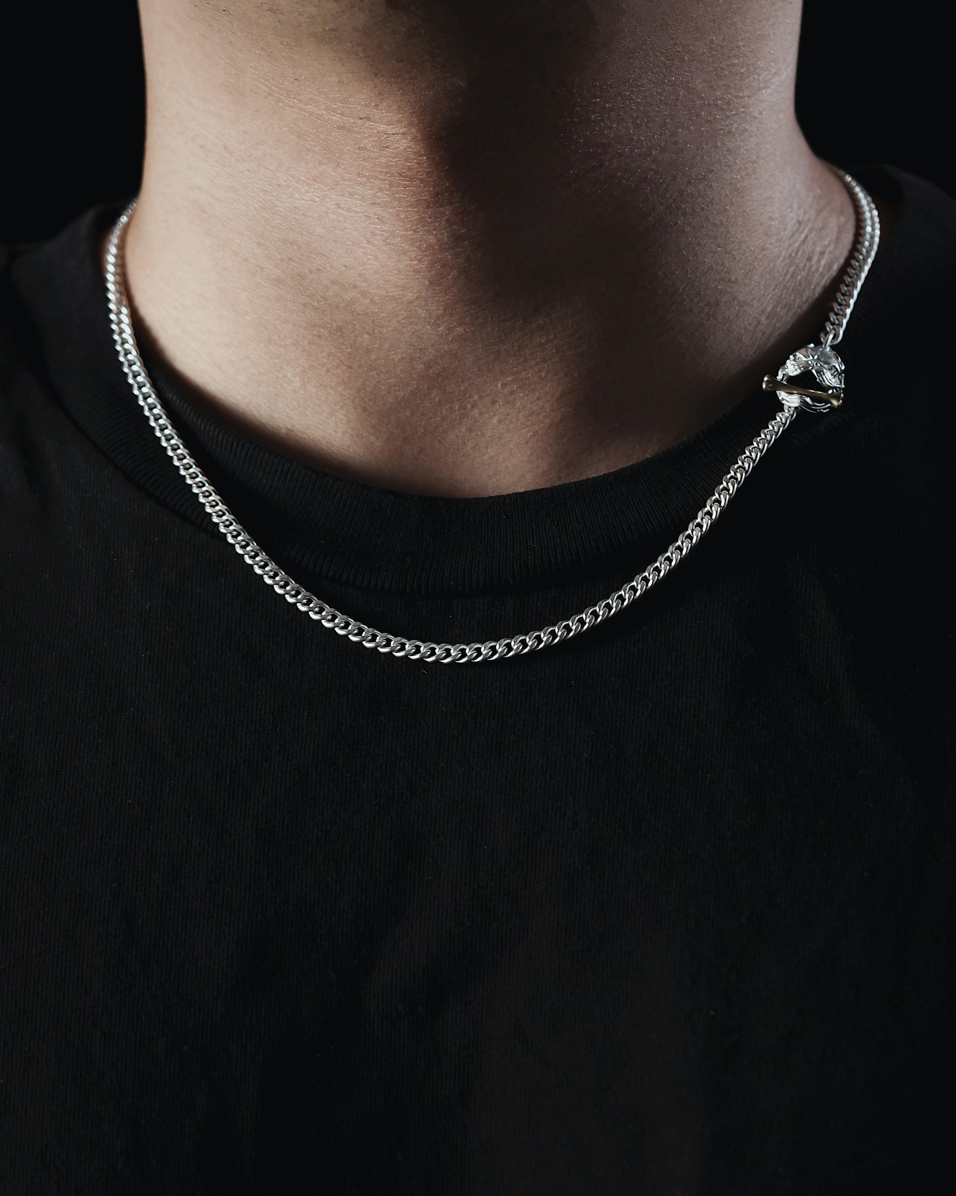 Close-up of a minimalist silver chain necklace resting on a matte black turtleneck, capturing the essence of bold yet refined streetwear.