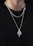 A person is wearing multiple silver chains around their neck against a black background. The most prominent chain features an intricately designed snake pendant with a textured surface.