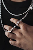 Close-up of hands adorned with black leather gloves holding a delicate silver chain.