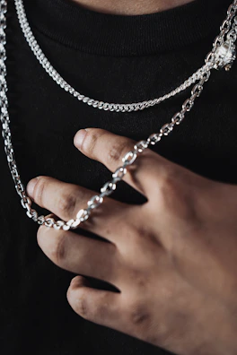 Close-up of hands adorned with black leather gloves holding a delicate silver chain.