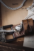 A close-up of a detailed leather strap with silver chains and a metallic skull emblem. The background includes vintage paper documents, partly in German, adding a rustic and historical ambiance.