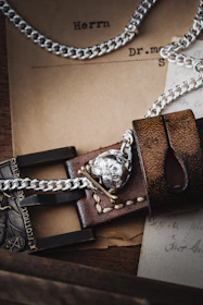 A close-up of leather cuffs and chains resting on a black surface, hinting at restraint and devotion.