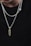 A close-up view of two silver chains with pendants against a plain black background. One pendant is a gold, segmented piece, while the other is a silver heart. The chains have a shiny, polished appearance.