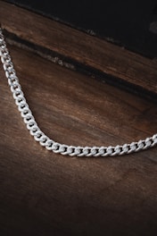 A stylish silver chain resting on a wooden surface with natural light