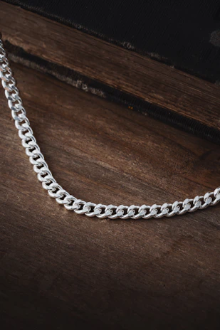 Artistic shot of a solid silver chain coiled loosely on a rustic wooden surface.