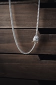 A silver necklace with a pendant, hanging against a background of textured, dark wooden drawers. The necklace has a sleek, twisted chain that adds a touch of elegance.