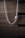 A silver necklace with a pendant, hanging against a background of textured, dark wooden drawers. The necklace has a sleek, twisted chain that adds a touch of elegance.