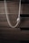 A silver necklace with a pendant, hanging against a background of textured, dark wooden drawers. The necklace has a sleek, twisted chain that adds a touch of elegance.