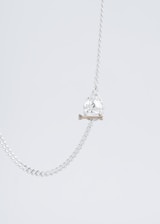 A silver chain necklace with a pendant featuring a skull and crossbones design. The pendant has intricate details and appears to be made of silver with a small gold accent on the crossbones. The background is a plain, light grey color.