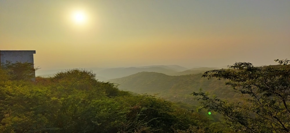 the sun is setting over the mountains and trees