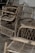 A collection of rustic, woven wicker chairs arranged on a wooden floor. The chairs have curved armrests and a woven back and seat design, giving a vintage and artisan feel.