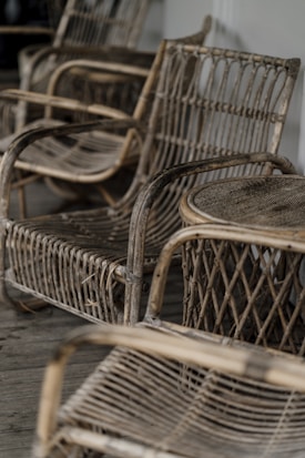 A collection of rustic, woven wicker chairs arranged on a wooden floor. The chairs have curved armrests and a woven back and seat design, giving a vintage and artisan feel.