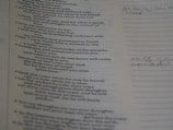 A close-up view of a page from a book or document with text printed on it. The text appears to be from a religious or philosophical book, possibly a Bible. Some handwritten notes are visible on the right side of the page, written on lined paper.