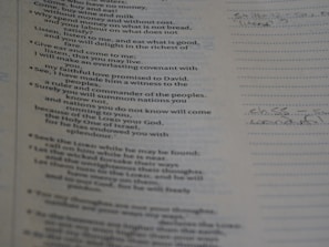 A close-up view of a page from a book or document with text printed on it. The text appears to be from a religious or philosophical book, possibly a Bible. Some handwritten notes are visible on the right side of the page, written on lined paper.