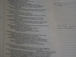 A close-up view of a page from a book or document with text printed on it. The text appears to be from a religious or philosophical book, possibly a Bible. Some handwritten notes are visible on the right side of the page, written on lined paper.